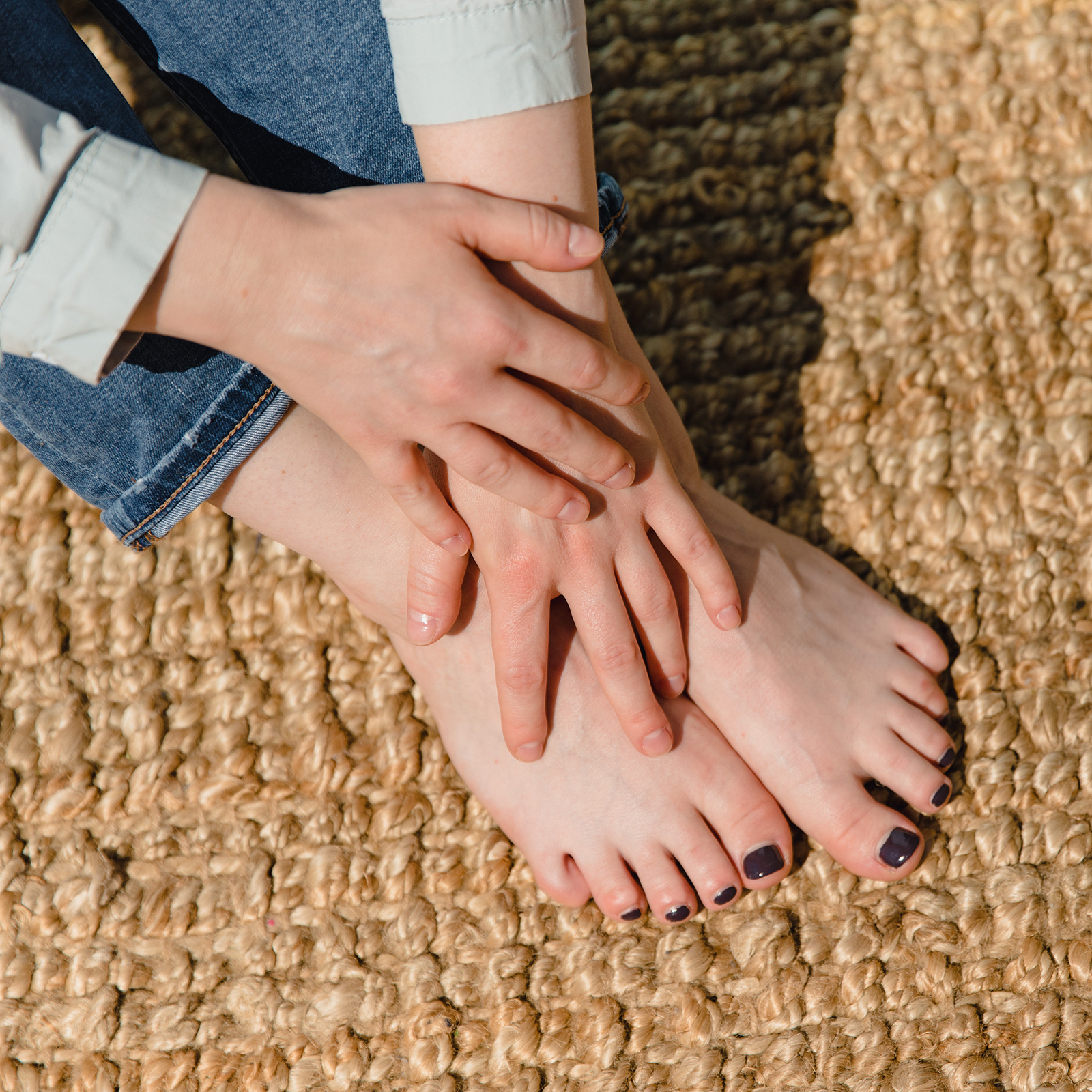 bare hands atop bare feet resting on natural material outdoor rug