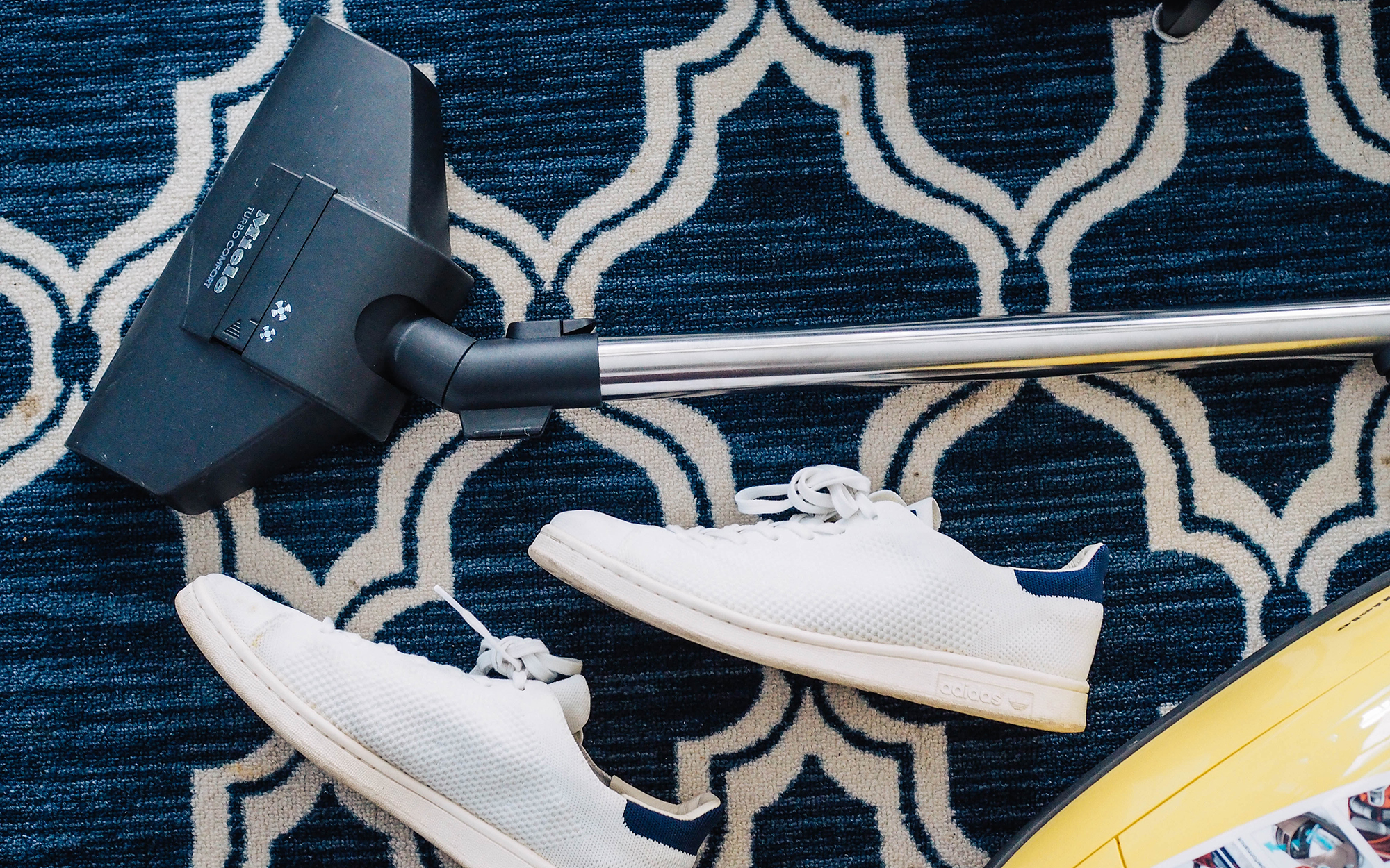 white sneakers and vacuum cleaner on blue and white rug