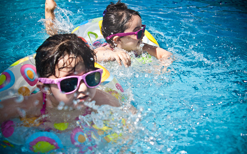 children in sunglasses using colorful pool rings to paddle in the water