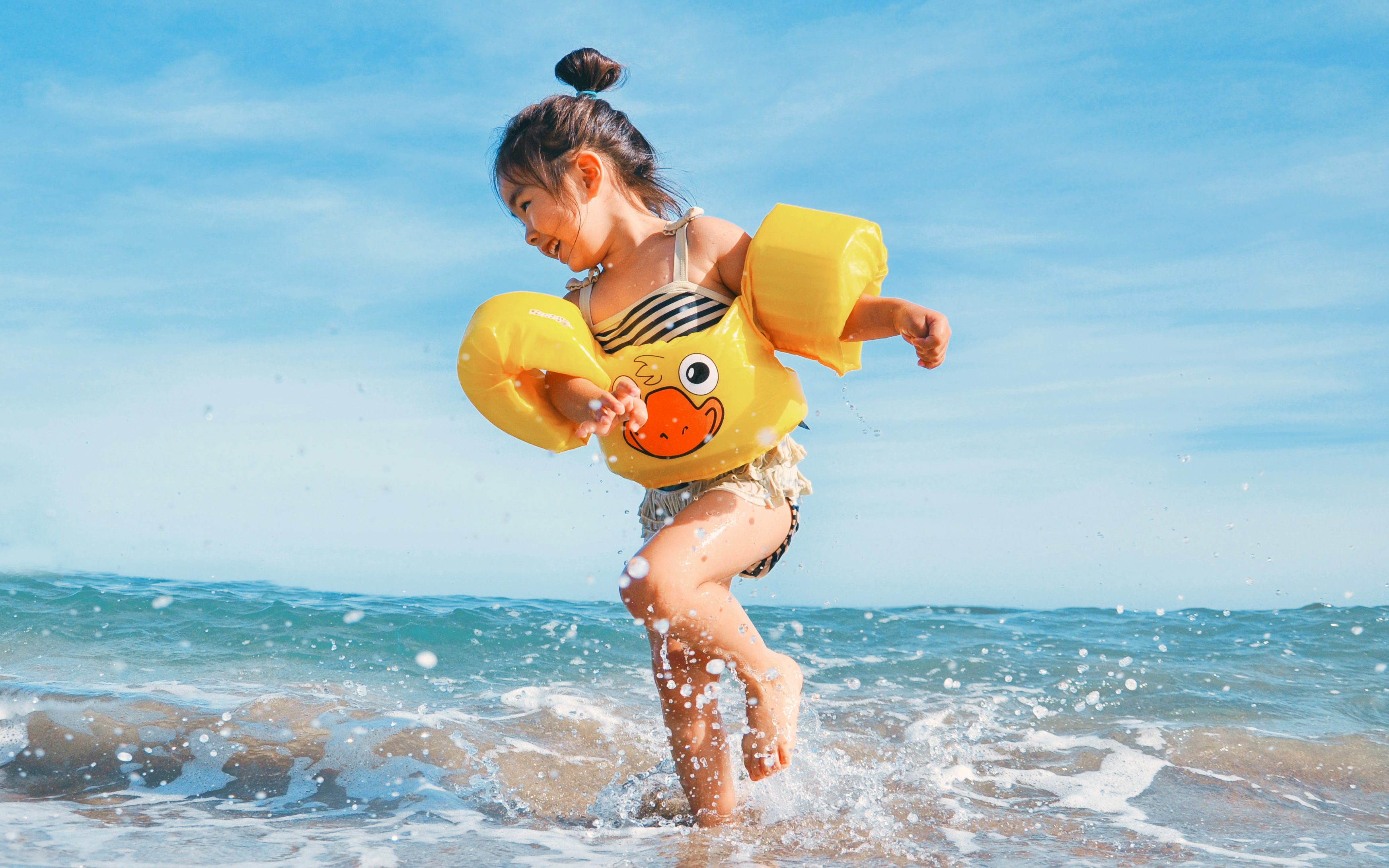 little girl with yellow arm floats playing in ocean surf