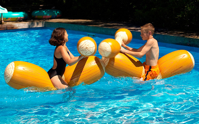 kids playing on pool jousting logs with pair of inflatable boppers