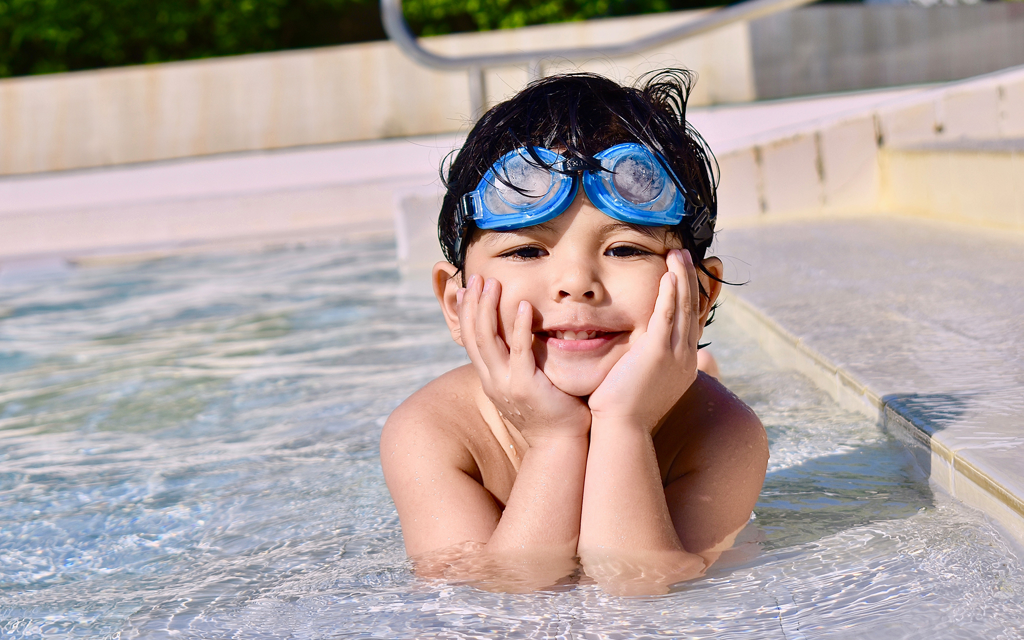 small boy wearing goggles posing at poolside