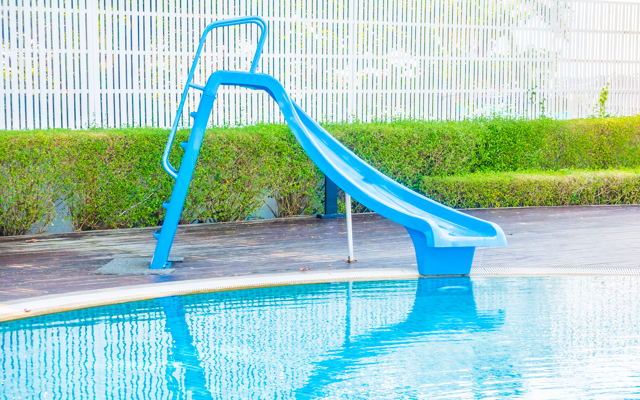 blue swimming pool slide in front of calm swimming pool