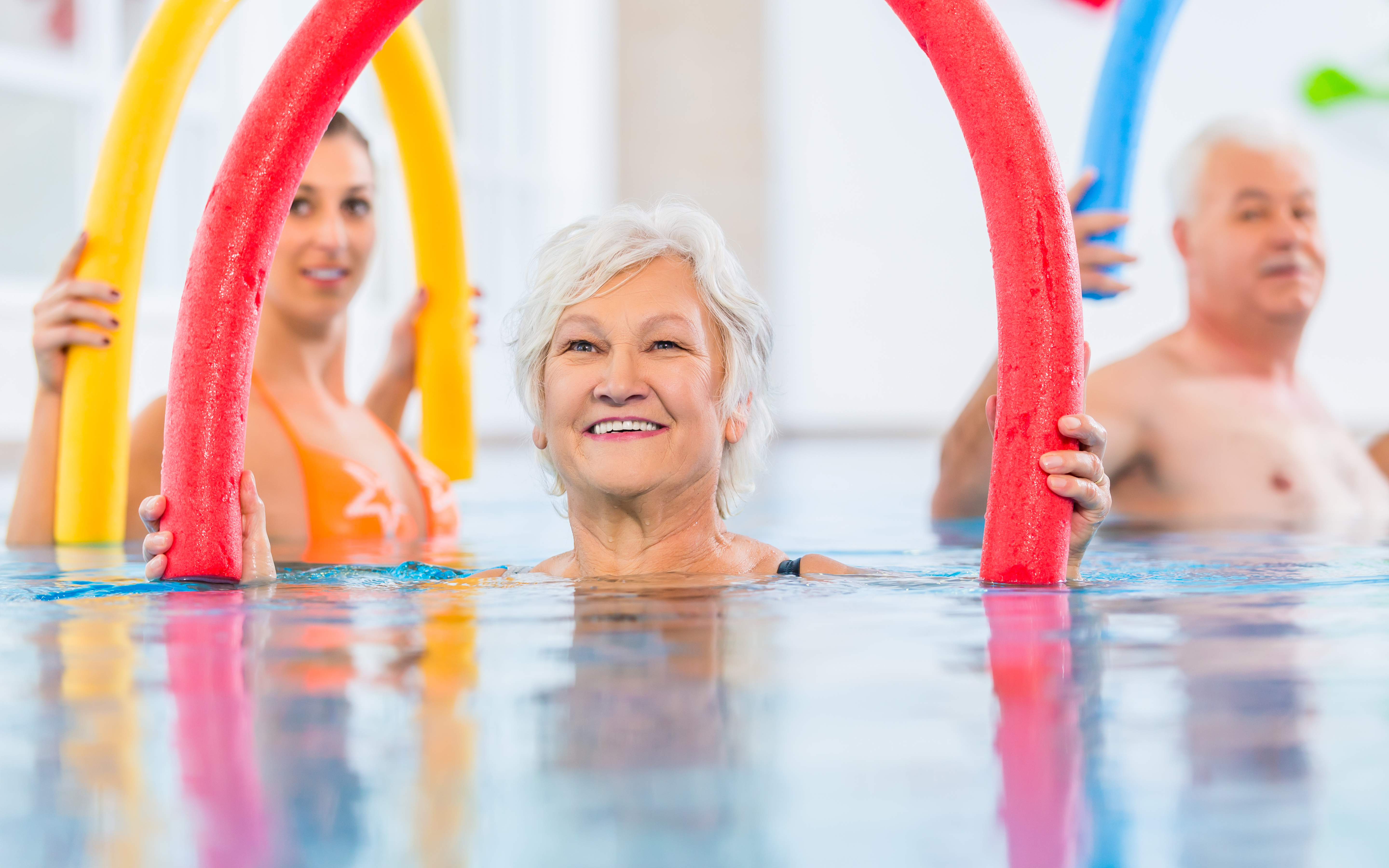 seniors using colorful pool noodles during a water exercise class