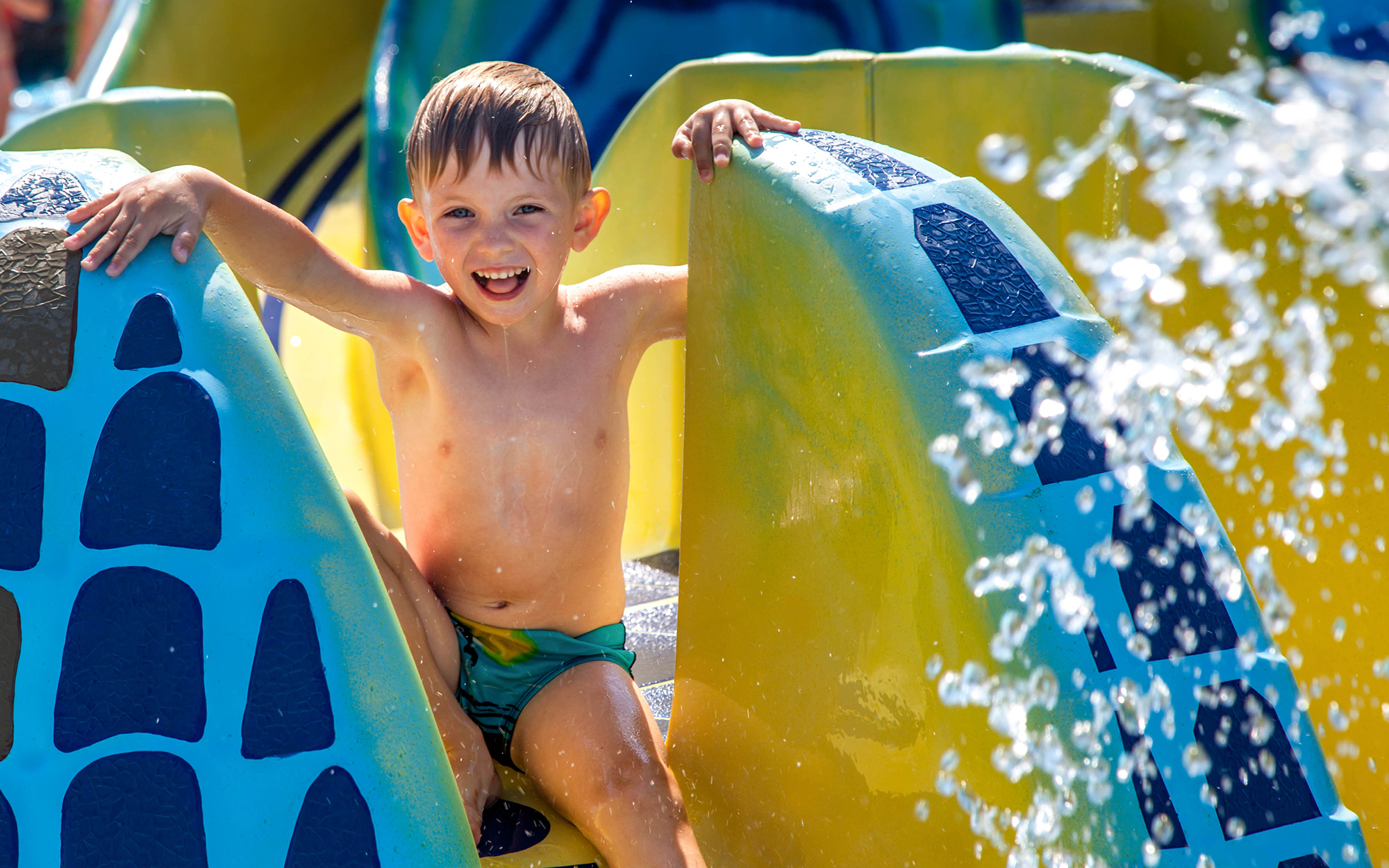 young boy on blue and yellow water slide