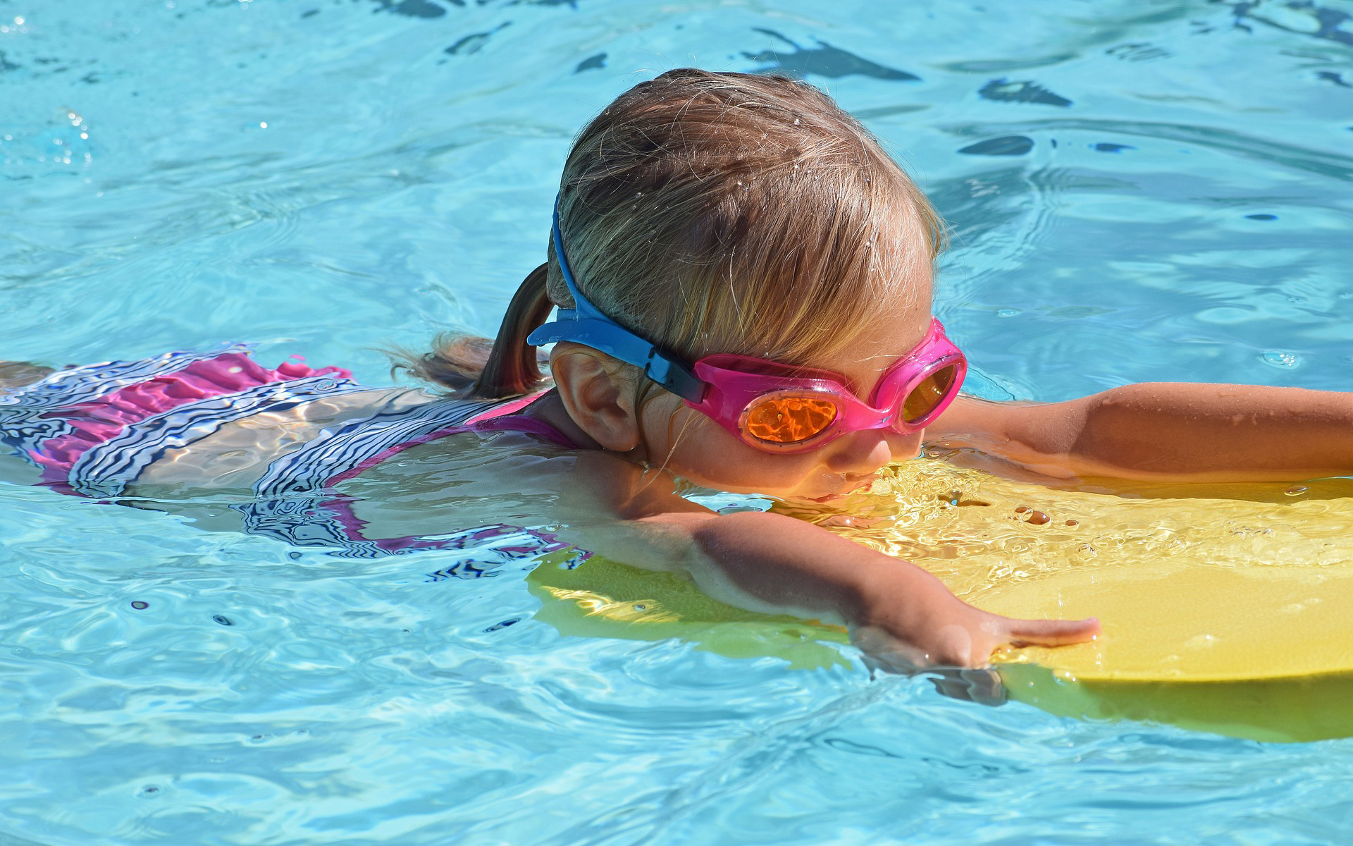 child with goggles using kickboard in pool
